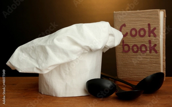 Fototapeta Chef's hat with spoons and cookbook on table on brown