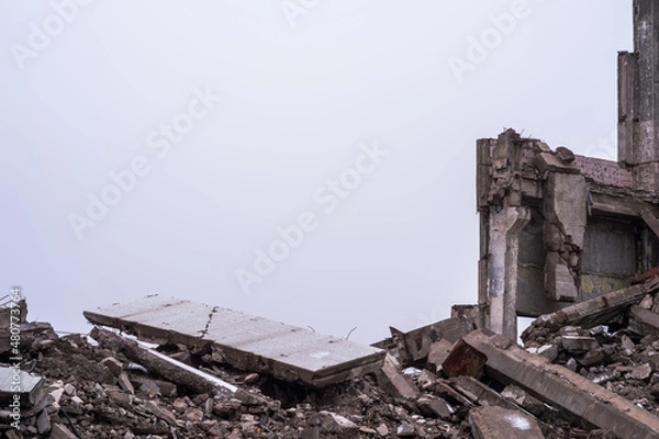Fototapeta A pile of large concrete fragments against the background of the remains of the building and the gray sky. Background