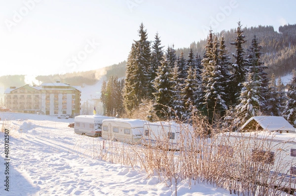 Fototapeta Trailers at a ski resort in the snowy mountains against the background of wooden hotels covered with snow