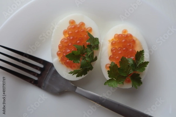 Fototapeta Red caviar with parsley lies on boiled and chopped eggs on a plate, top view.
