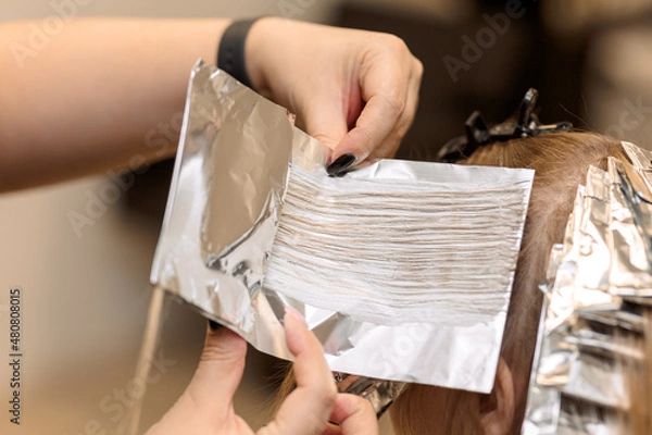 Obraz close-up. 
the hairdresser applies dye to a strand of hair and wraps it in foil