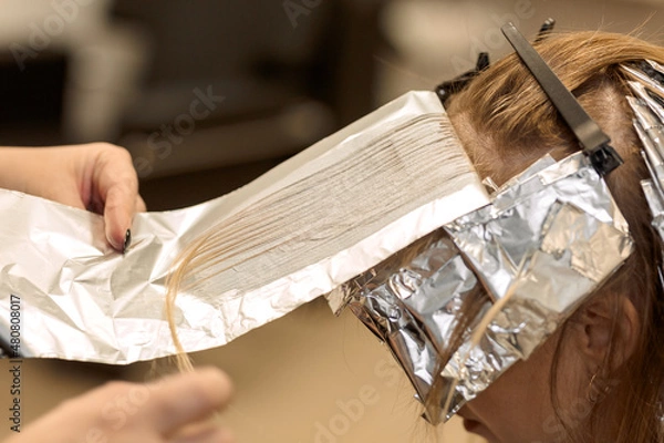 Obraz close-up. 
the hairdresser applies dye to a strand of hair and wraps it in foil