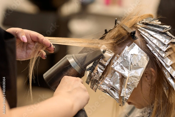 Obraz close-up. a hairdresser using a hair dryer selects strands of hair for dyeing air touch
