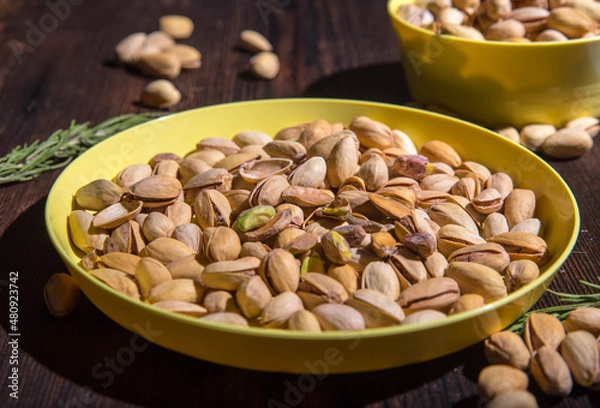 Fototapeta Pistachio nuts in a yellow bowl on a wooden background, side view, copy space