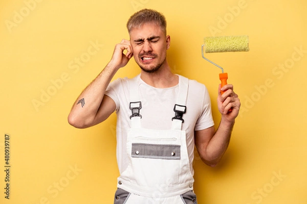 Obraz Young painter man isolated on yellow background covering ears with hands.