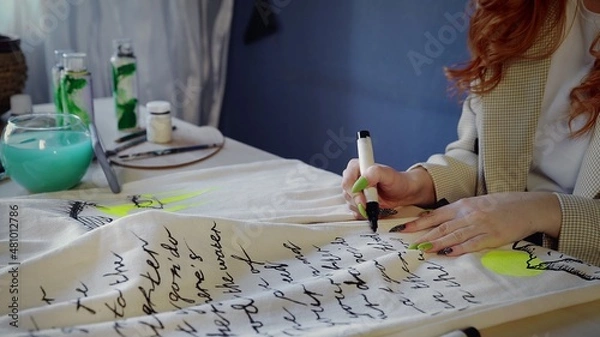 Obraz Close-up of a beautiful red-haired girl drawing with multicolored paints on clothes. Handmade work