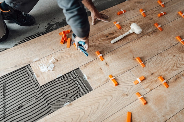 Obraz Professional tiler placing level in position with lash tile leveling system and clamp level ceramic tiles. Flooring and tiling concept.