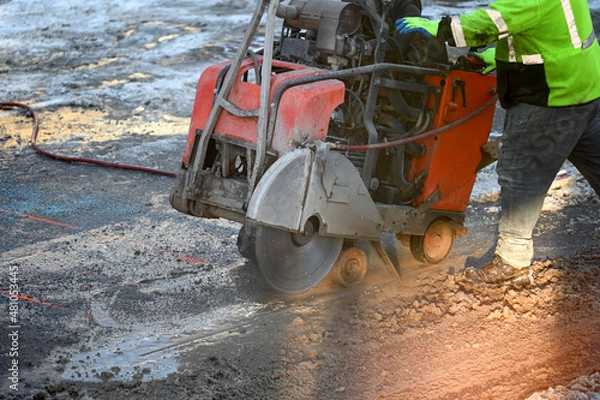 Obraz Worker using an asphalt saw cutting machine in winter