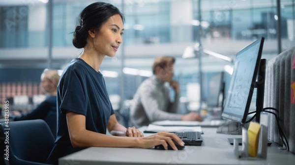 Fototapeta In Big Corporate Office: Portrait of Confident Beautiful Asian Manager Using Computer, Businesspeople and Experts Working Around Her, Analysing Statistics, Commerce Data, Marketing Plans.