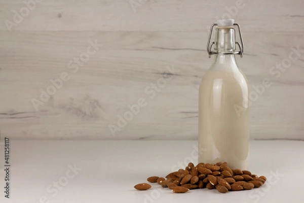 Fototapeta A bottle with alternative dairy free almond milk and nuts on light background. Lactose free beverage