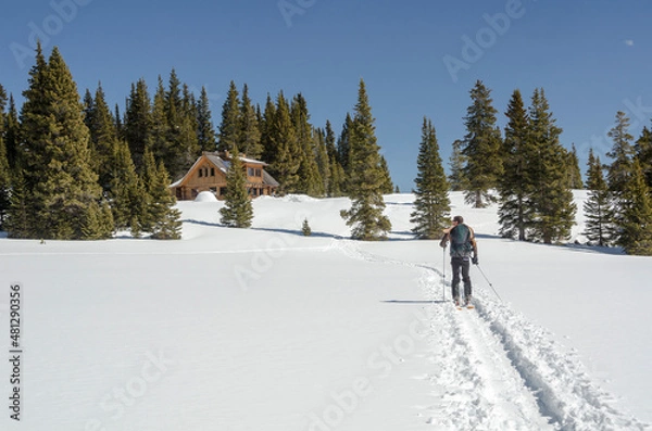 Fototapeta Skiing towards a backcountry cabin in winter
