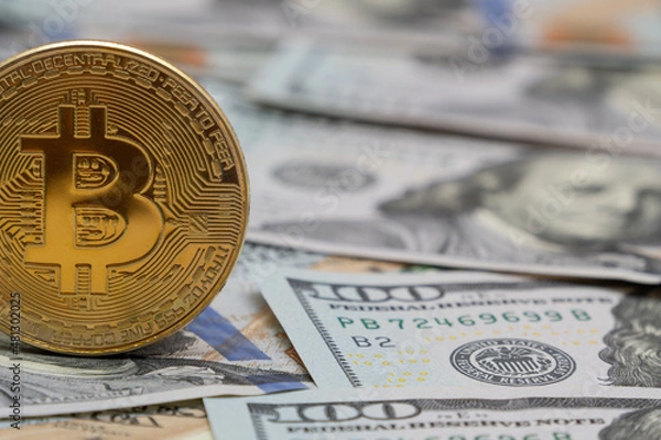 Fototapeta Close-up of a golden shiny bitcoin cryptocurrency coin on US dollar bills. The concept of the future of electronic decentralized money, online payments and electronic cryptocurrency.