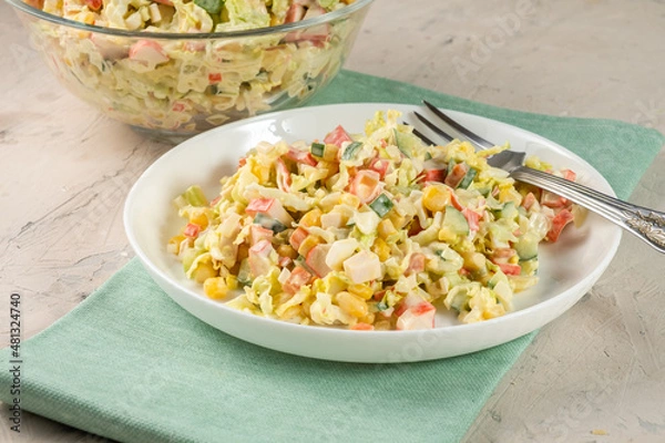 Obraz Classic crab salad with surimi sticks and vegetables in a white plate on a blue rag.