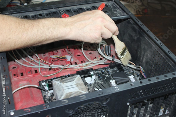 Fototapeta A man cleans a computer from dust with a brush, a close-up of a dirty system unit of a personal computer