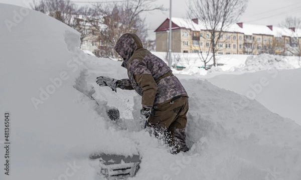 Fototapeta a man digs his car out of the snow captivity.car covered with snow after a heavy snow storm