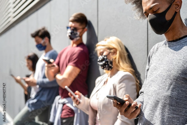 Fototapeta People using smartphone covered by mask on omicron variant wave - Worried guys and girls watching news on mobile devices - College students breaking at university campus - Focus on lower right phone