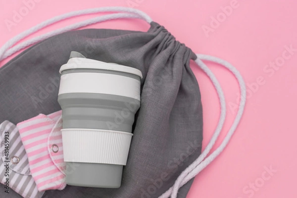 Fototapeta Trendy environmental friendly reusable cup. Folded reusable cotton menstrual pads. Grey shopping mesh bag. Concept of conscious consumption. Alternatives to disposables.