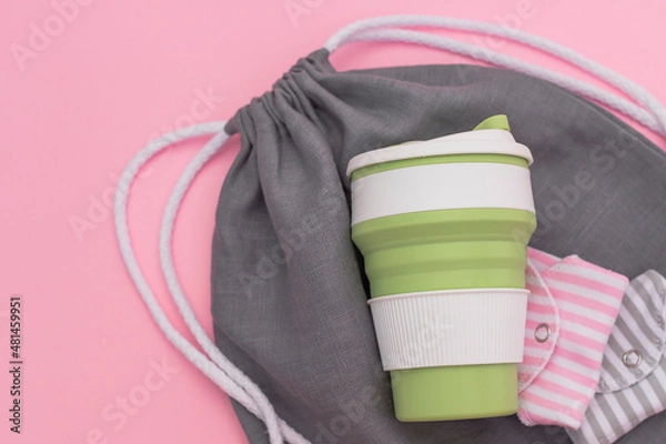 Fototapeta Trendy environmental friendly reusable cup. Folded reusable cotton menstrual pads. Grey shopping mesh bag. Concept of conscious consumption. Alternatives to disposables.