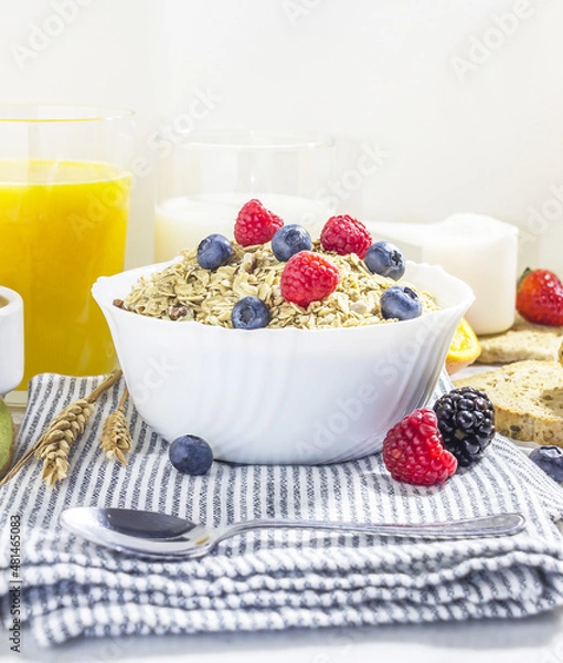 Fototapeta healthy breakfast of granola with blueberries and raspberries in a white porcelain bowl, with fruit, milk, coffee and wheat toast. front view
