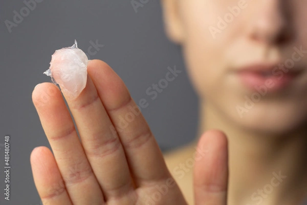 Fototapeta A young woman is applying petroleum jelly to her face. Concept of slugging.