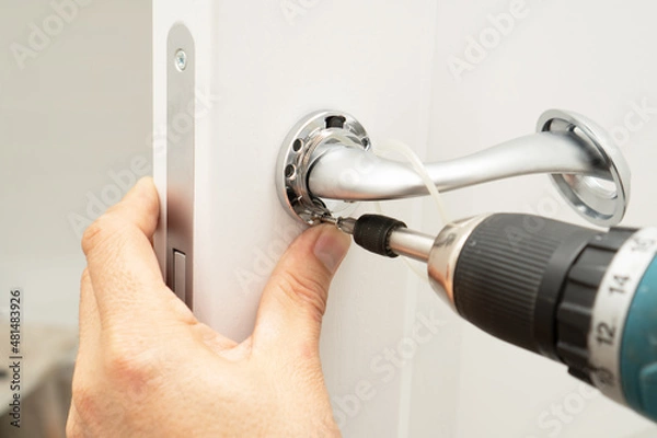 Fototapeta Service man installing magnetic lock and a door handle on an interior door using a screwdriver.