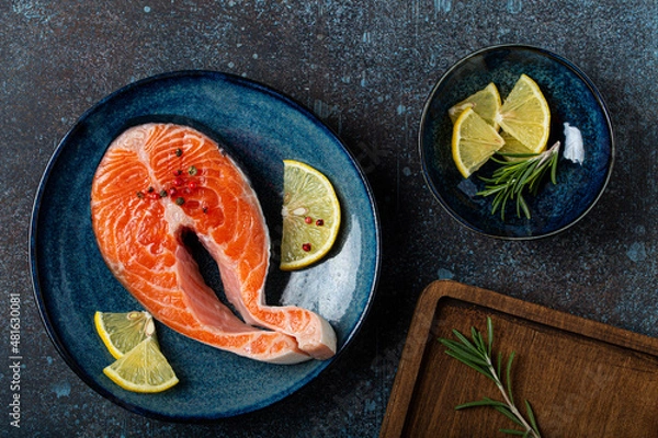 Fototapeta Uncooked raw fresh fish salmon steak top view on plate rustic dark concrete stone background with rosemary, lemon wedges and spices, delicacy healthy fish cooking and nutrition concept flat lay