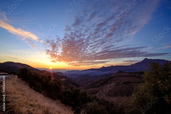Fototapeta Beautiful cloudscape sky with moving cirrus and cirrocumulus clouds by the wind on a beautiful sunrise mountain landscape with yellow sun shining on the horizon