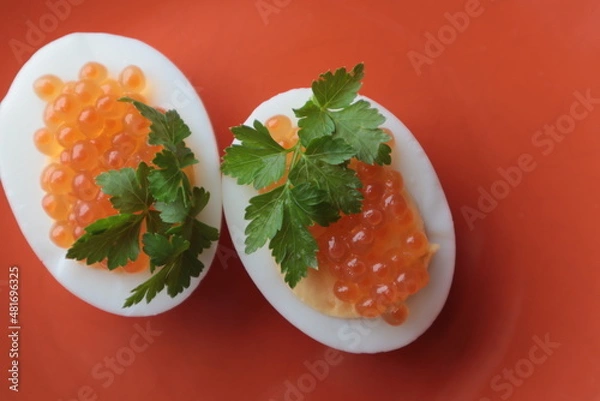 Obraz Red caviar with parsley lies on boiled and chopped eggs on a plate, top view.	