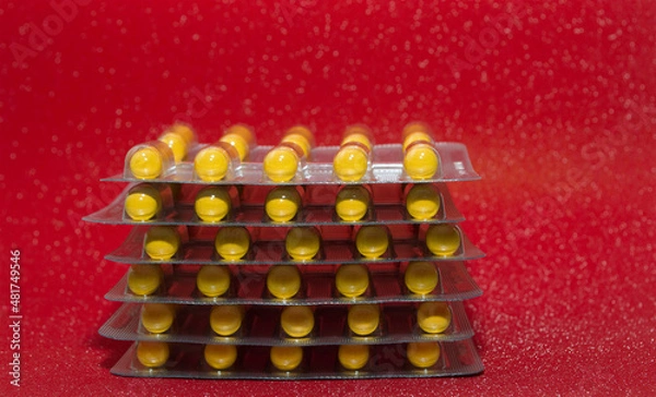 Obraz yellow capsules tablets in a silver blister on a red background