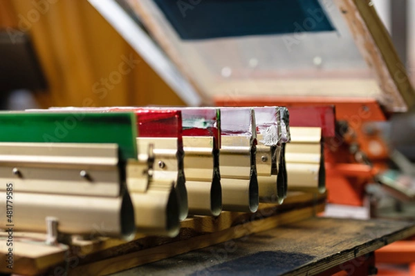 Fototapeta serigraphy production. squeegees on wooden shelve of the print screening apparatus. printing images on t-shirts by silk screen method in a design studio