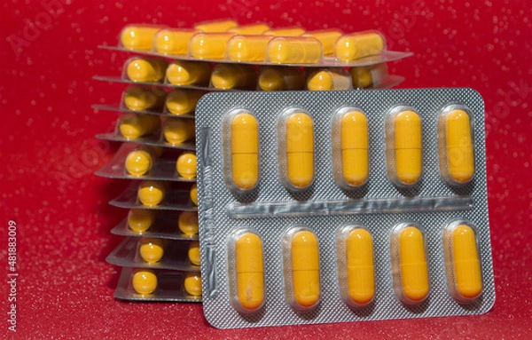 Obraz yellow capsules tablets in a silver blister on a red background