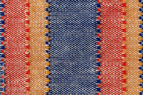 Fototapeta Macro texture of plain weave fabric. Striped cloth background of red, blue, orange and white colors. Textile canvas surface close-up. Design element of colorful woven fabric. Weft and warp.