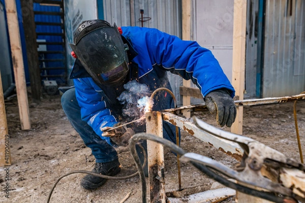Fototapeta a masked welder does his job, a welder cooks metal