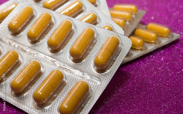 Obraz yellow capsules pills pills in a silver blister on a crimson background close-up