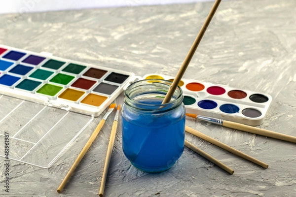 Obraz watercolor paints a jar of water and brushes for drawing on a gray textured surface