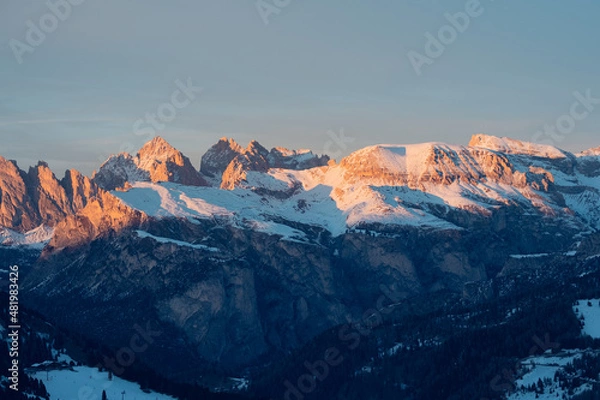 Fototapeta Mountains covered with snow and lit red by the sunset light