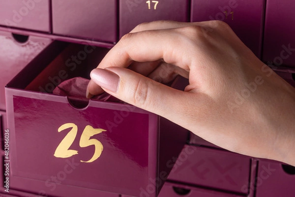 Fototapeta A woman's hand with a manicure opens the cell number 25 in the advent calendar. The girl takes out a gift in wrapping paper from the advent calendar.
