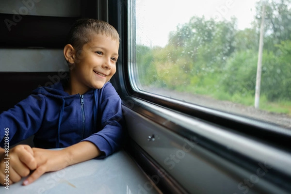 Fototapeta Child go the train at the window. Little passenger looks at the railway. Boy travels.