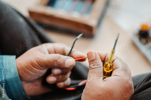 Fototapeta Closeup shot of hand of an Indian man fixing electronic item with screwdriver in his hand. Electrician fixes an electronic appliance. Repair background. 