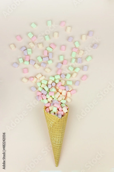 Obraz Yellow waffle cone with green, pink and yellow marshmallows on pastel background.