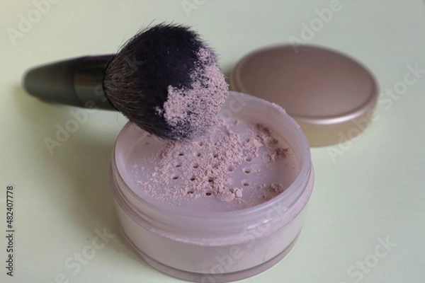 Obraz A soft brush with powder lies on a jar on a light surface.	