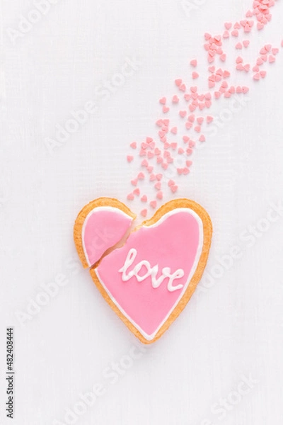 Fototapeta Broken heart shaped cookie with text LOVE is falling down like a comet, top view, flat lay