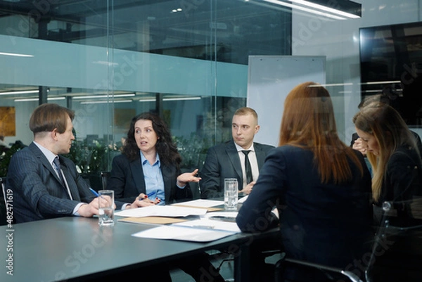 Fototapeta Business people in official wear sitting in office behind glass wall and discussing project, colleagues sharing ideas, teamwork of managers brainstorming, executives planning strategy