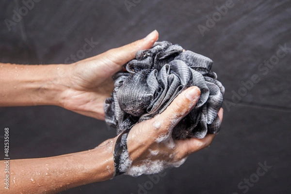 Fototapeta a woman's hand holds a black loofah as it suds up with soap and bubbles in a black tile shower