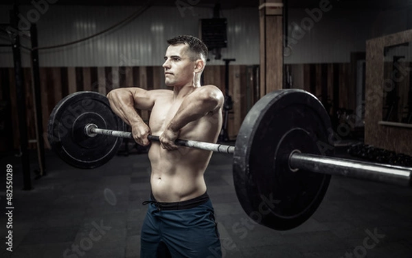 Obraz Athletic muscular man exercising with a heavy barbell in a modern health club. Bodybuilding and Fitness