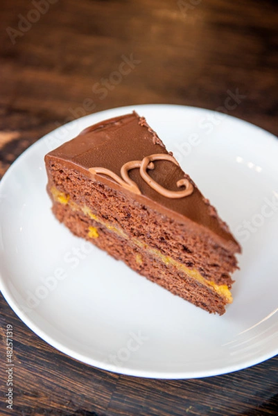 Fototapeta Chocolate Austrian dessert Sacher with apricot jam. One slice of traditional Sacher cake served on a white plate