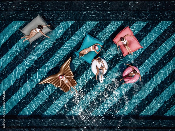Fototapeta Aerial drone view from above of a beautiful young ladies relaxing on inflatable mattress in the swimming pool and having fun in water on their vacation. Tropical holiday resort