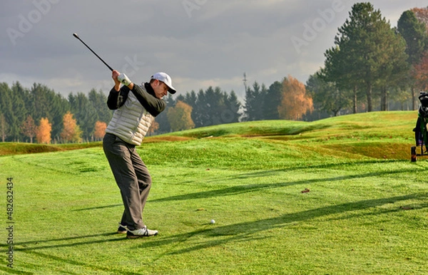 Fototapeta Golfer on a golf course in winter with wet grass, hitting the ball with a golf club.
