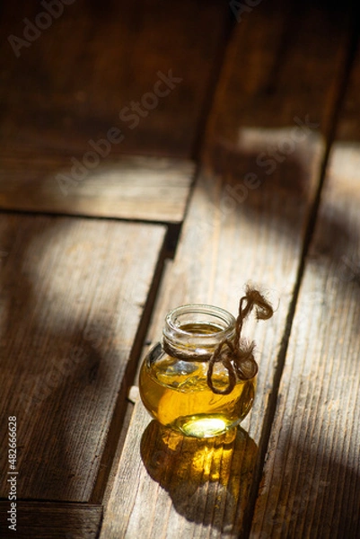 Fototapeta A small round glass jar of honey stands on an old shabby wooden table.