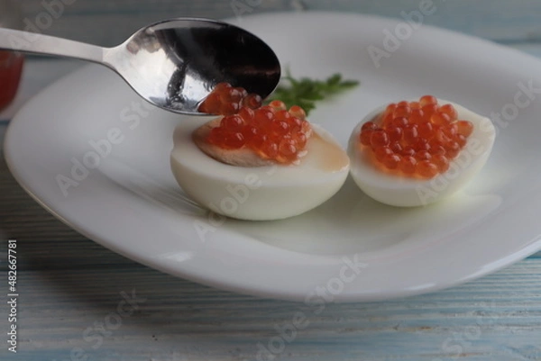 Obraz Put a spoonful of red caviar on boiled eggs, on a white plate.